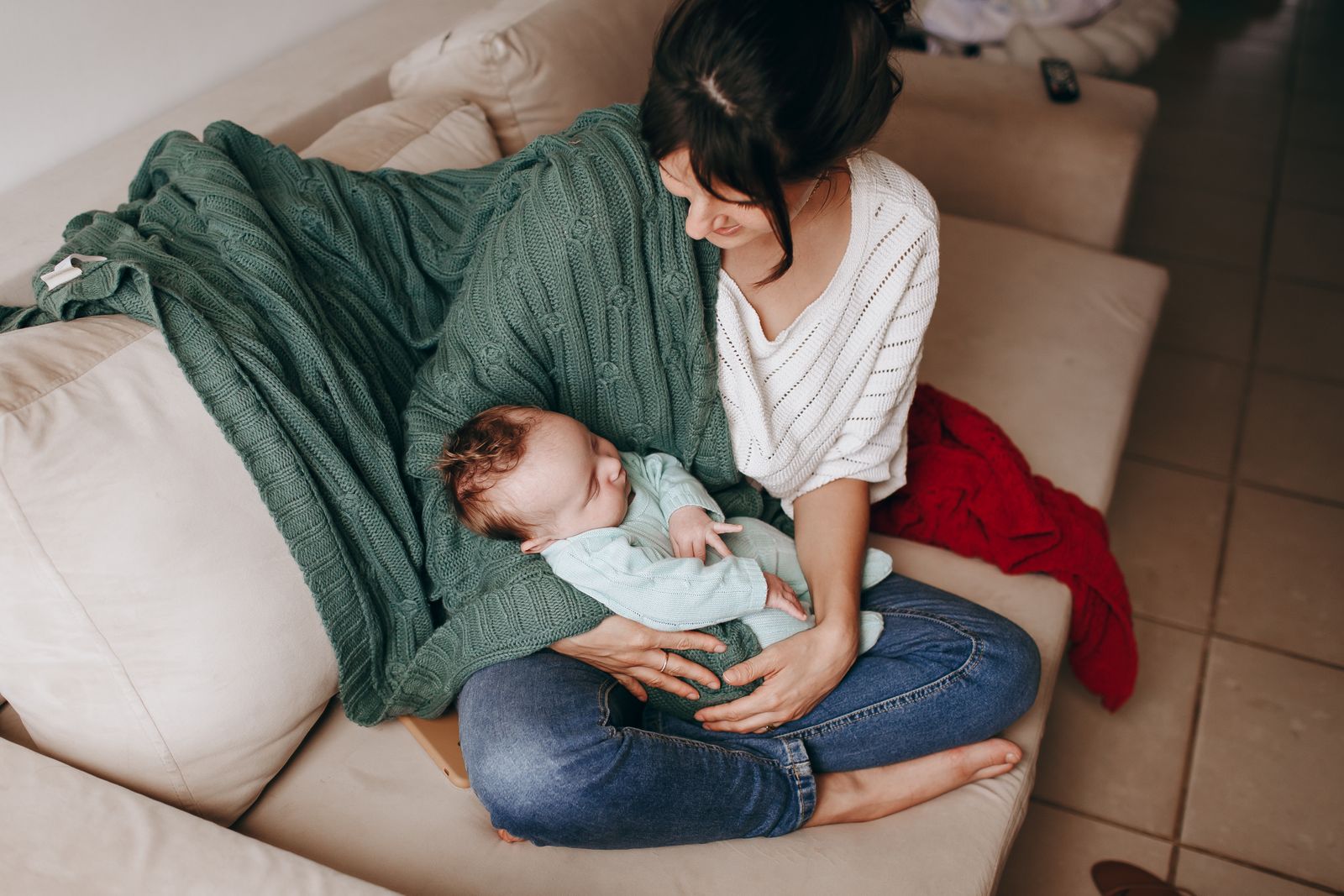 A mother in a cozy sweater cradling her calm newborn on the sofa