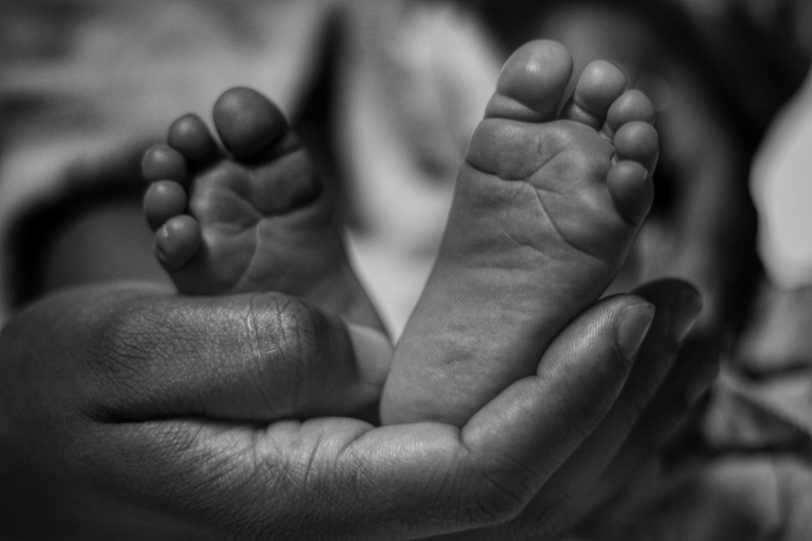 Black and white close-up of an adult hand gently cradling a baby's bare feet