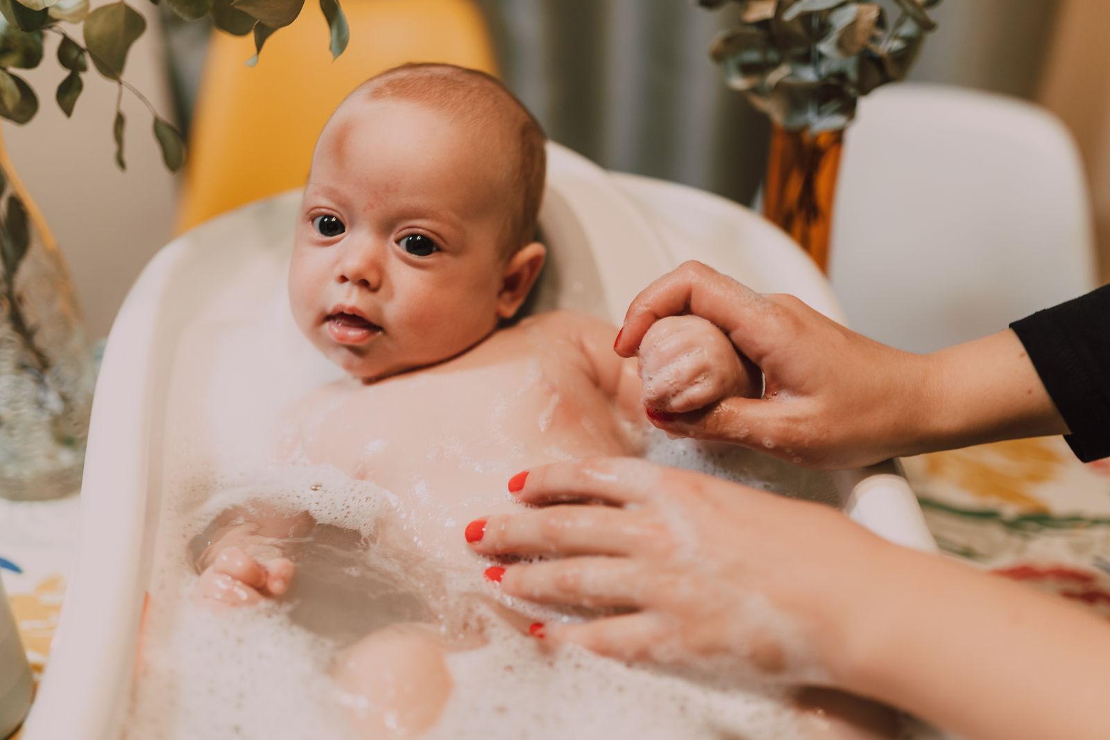A baby being gently washed in a small tub of warm, soapy water