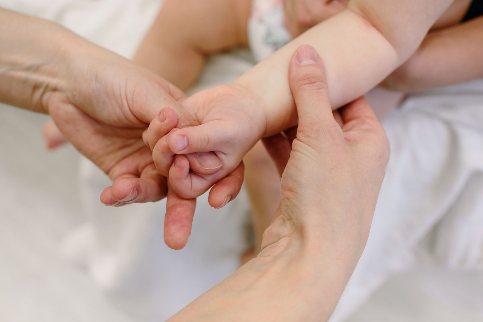 An adult's hands gently massaging a baby's arm and hand
