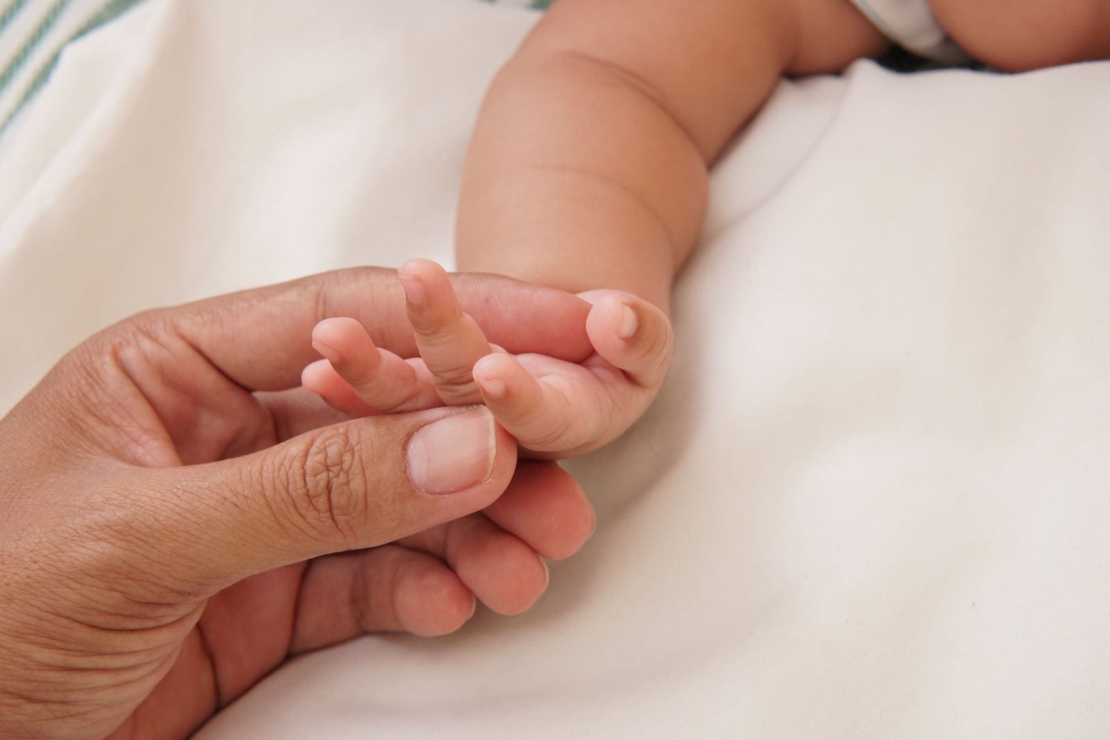 A parent's hand gently cradling their baby's tiny hand in soft light