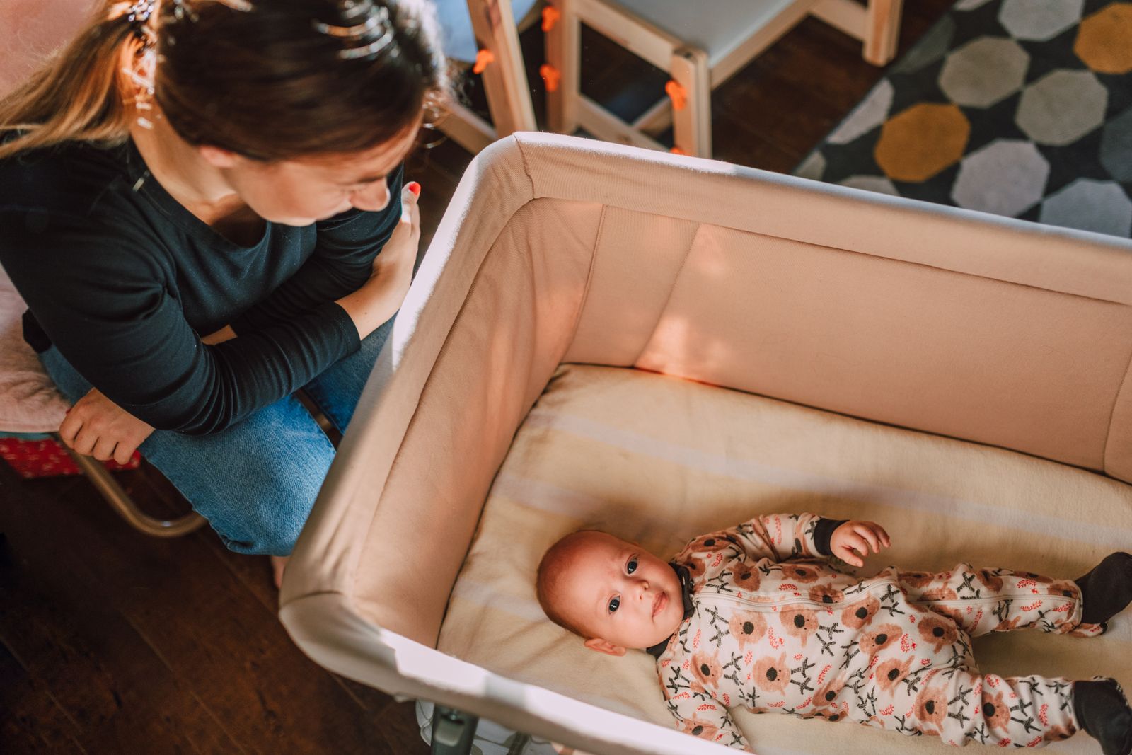A parent leans over a bedside bassinet, gently settling their baby down