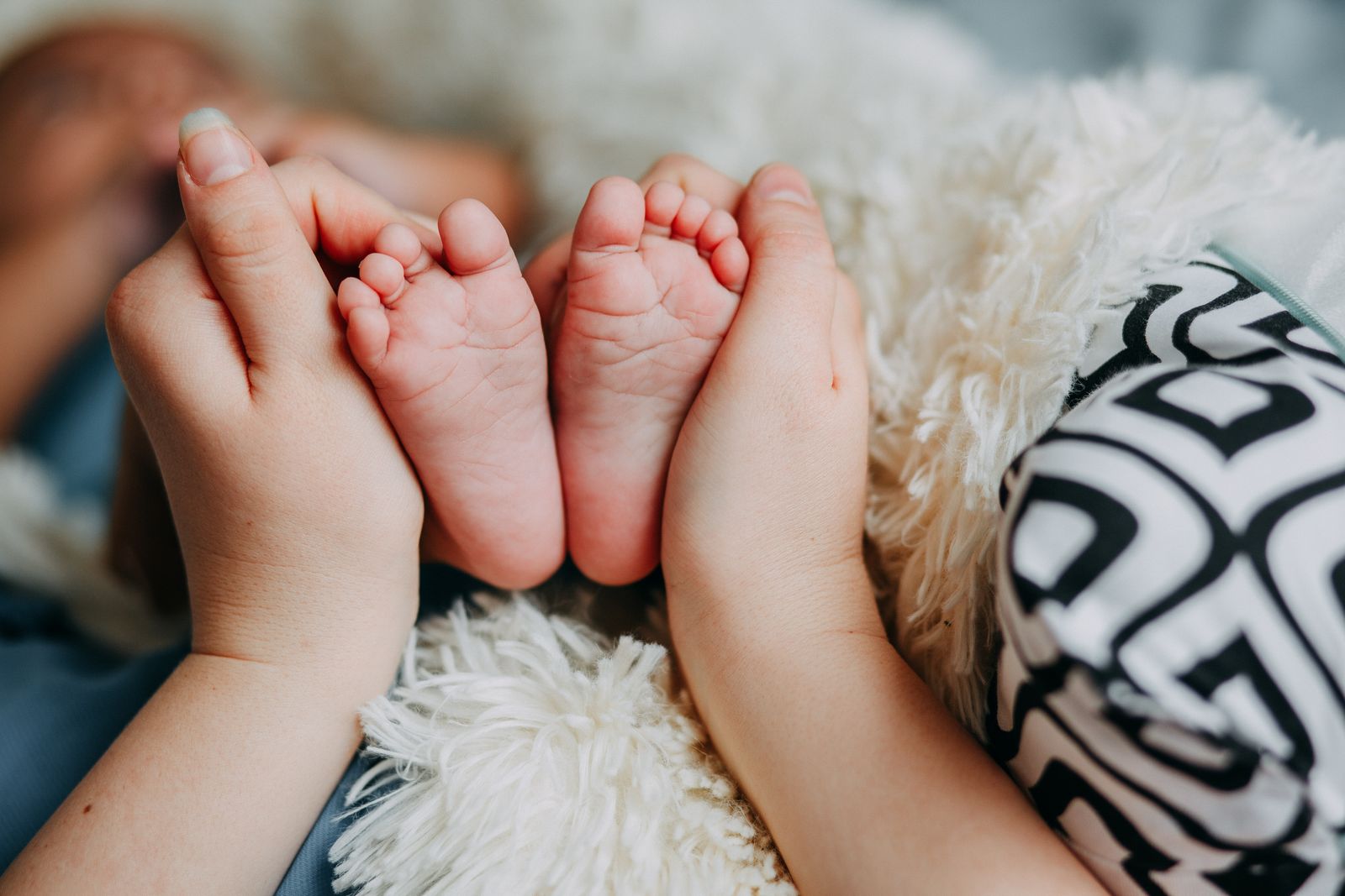 A parent's hand gently cradles a newborn's tiny foot, tender and close