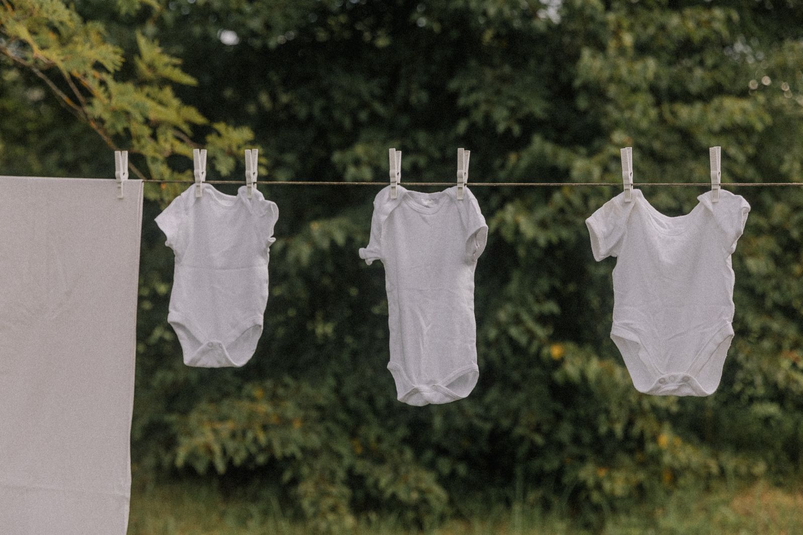 White baby onesies hanging on an outdoor clothesline to dry