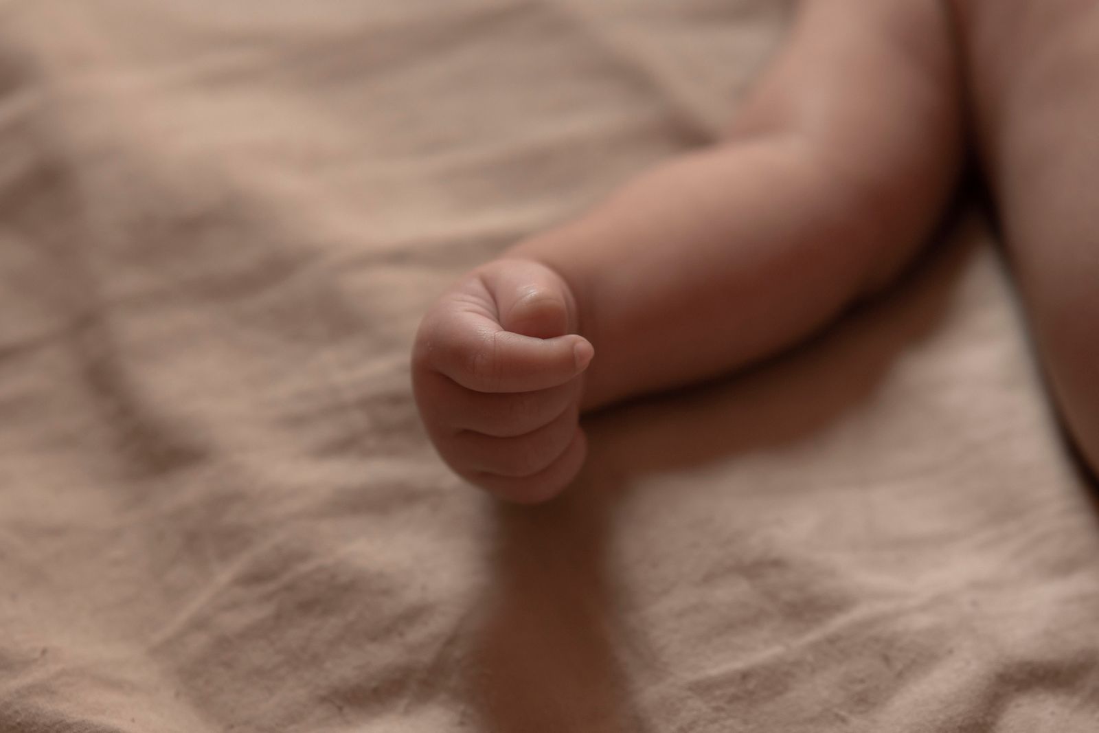 Close-up of a newborn's feet curled on a soft beige blanket