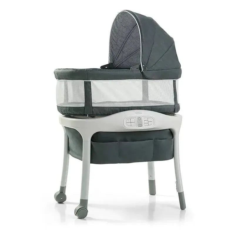 Graco Sense2Snooze bassinet in dark grey with a folding canopy, mesh sides, parent control panel, and a storage shelf, on a white background