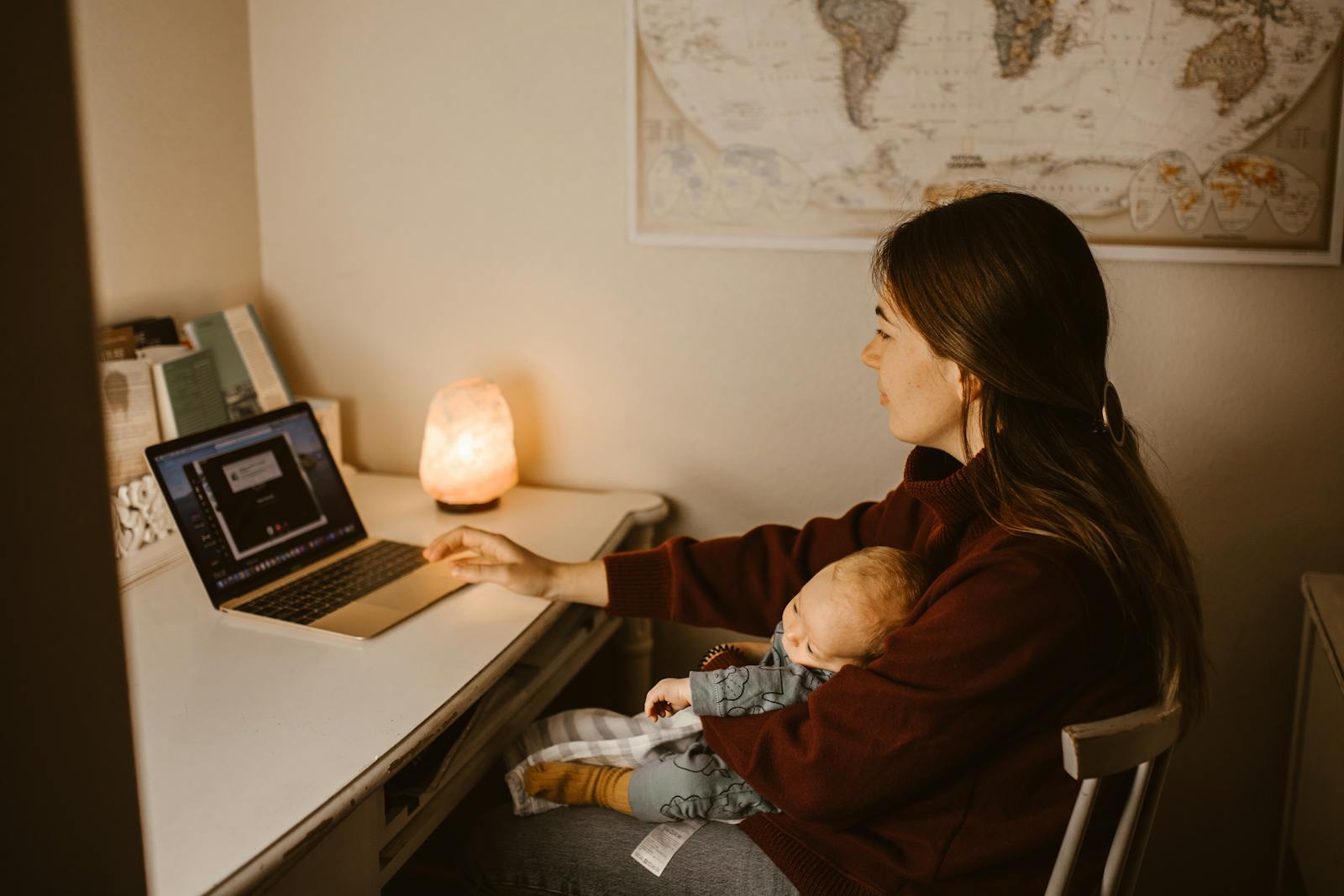 Working mom typing on laptop while baby sleeps in lap