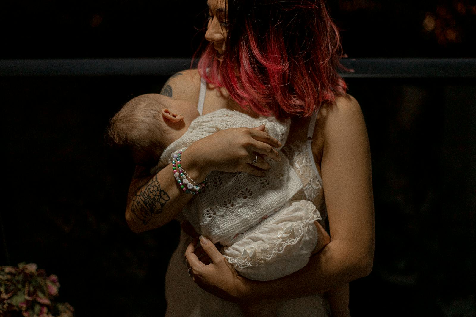 Modest mom holding sleeping baby cradled in white knit blanket, the early-weeks holding-and-rocking moment