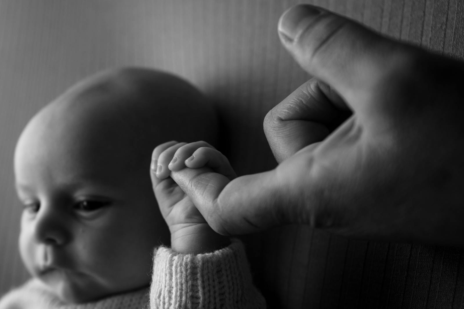 Black and white close-up of newborn hand gripping adult finger, the small moments that matter most