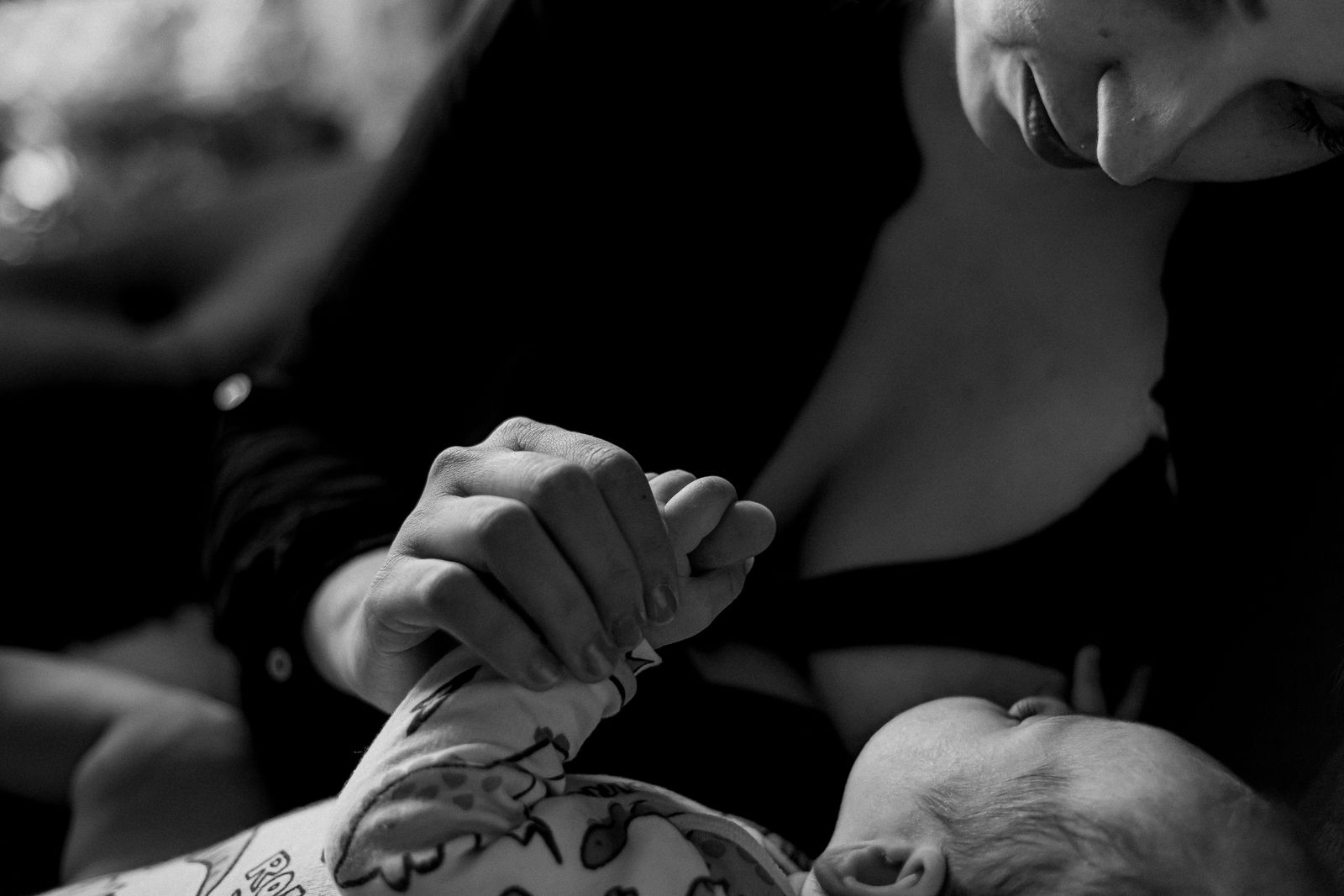 A baby's hand wrapped around a parent's finger while nursing, in soft black and white