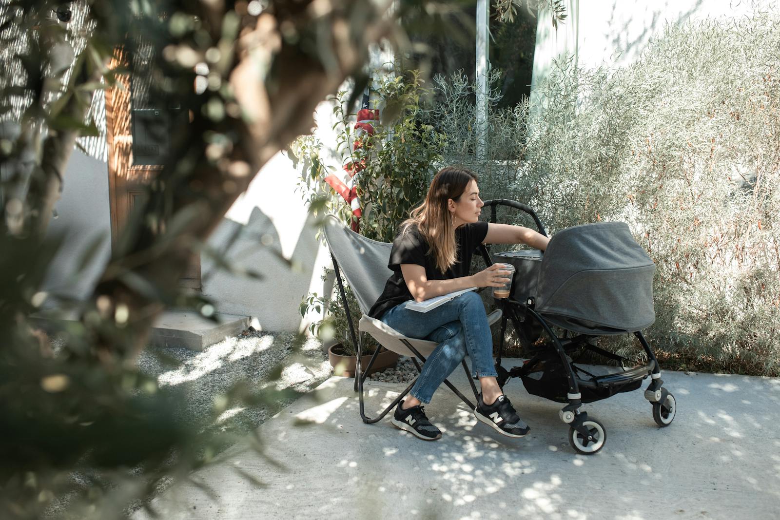 mom sitting outside with baby and stroller, drinking coffee on a calm patio