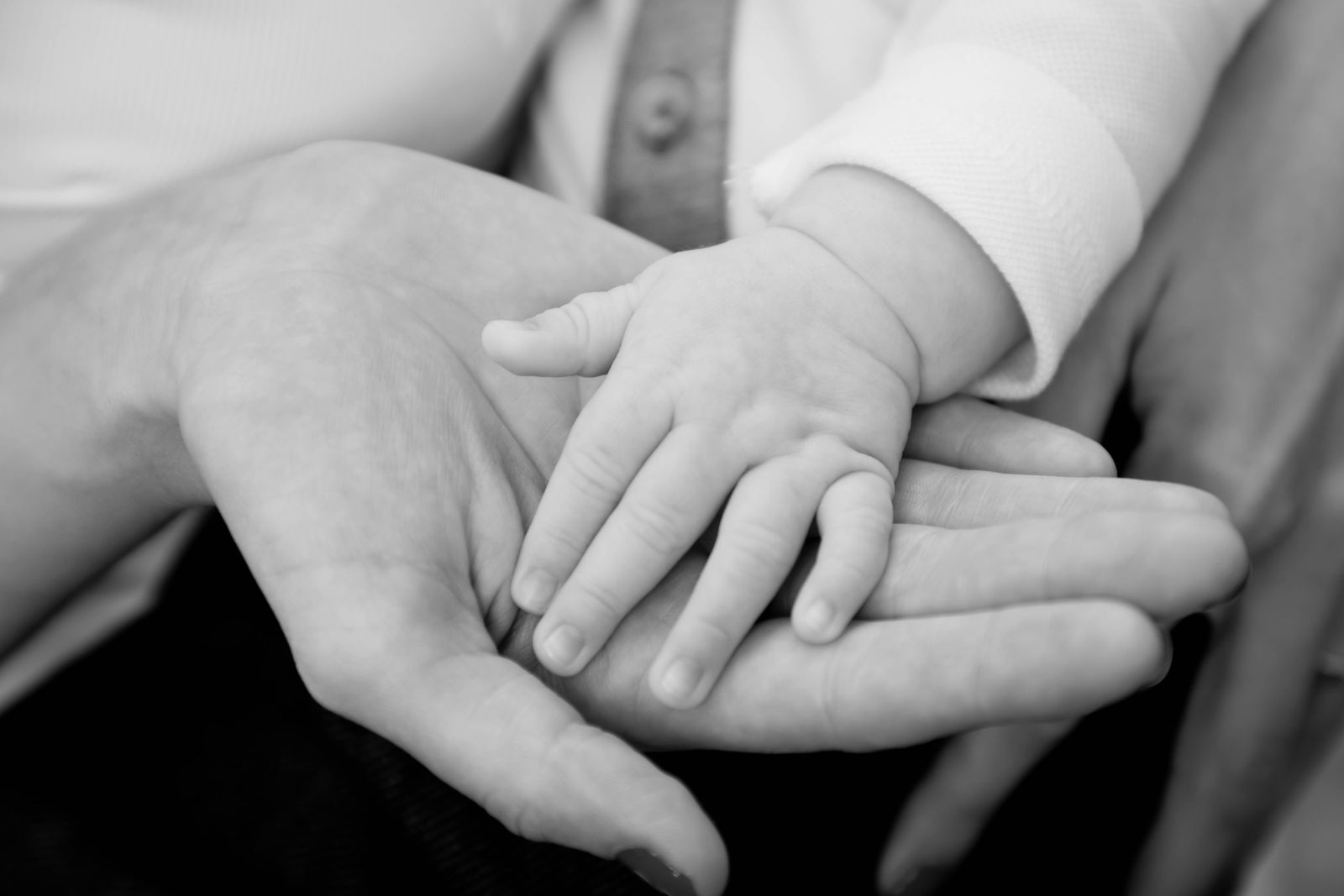 A baby's hand resting in a parent's open palm, in soft black and white