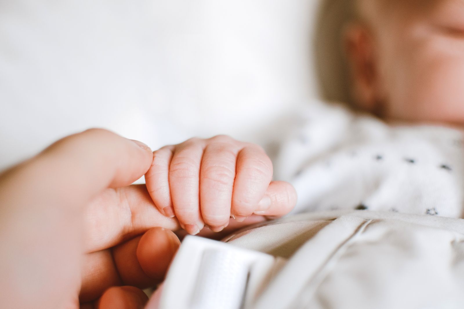 A newborn's hand gripping a parent's finger in a soft close-up