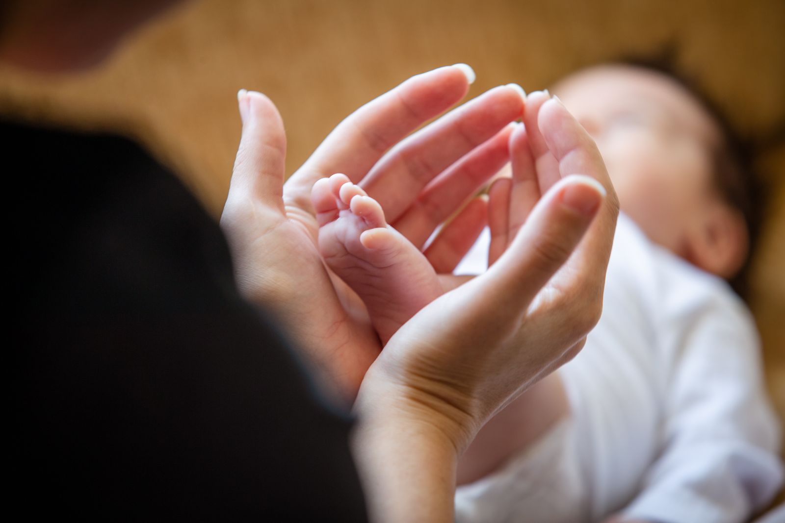 A parent's hands cradling their newborn's tiny foot in warm light