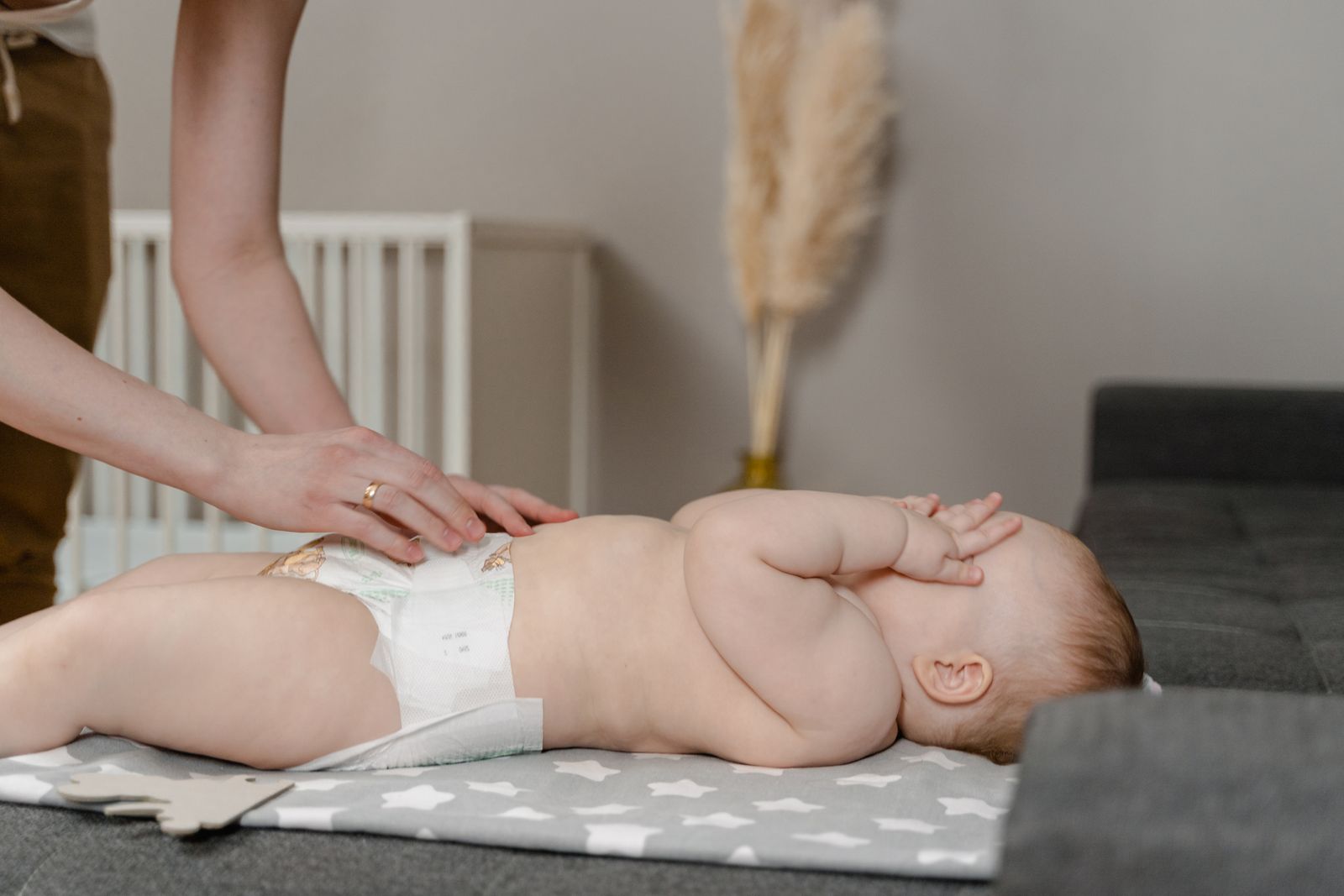 Mother fastening a clean diaper on a calm baby lying on a changing mat