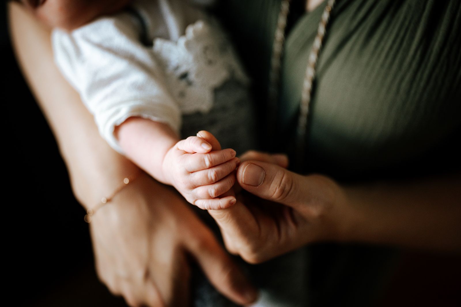 A baby's hand curled around a parent's finger