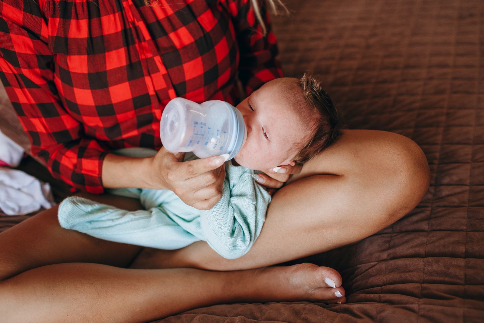 Mother in a striped shirt smiling while feeding her newborn a bottle of pumped milk
