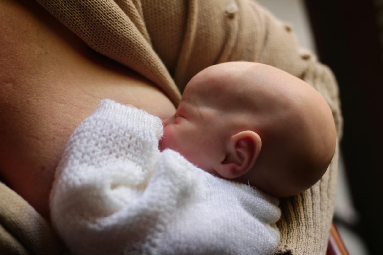 Newborn baby nursing in a cozy knit blanket during the first days of breastfeeding