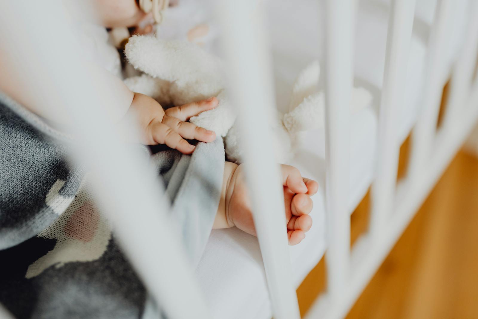 A peaceful sleeping baby in a crib with one little hand visible through the slats