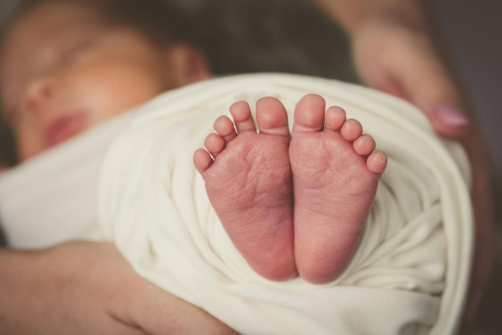 Tiny newborn feet resting on a cream wrap while baby sleeps