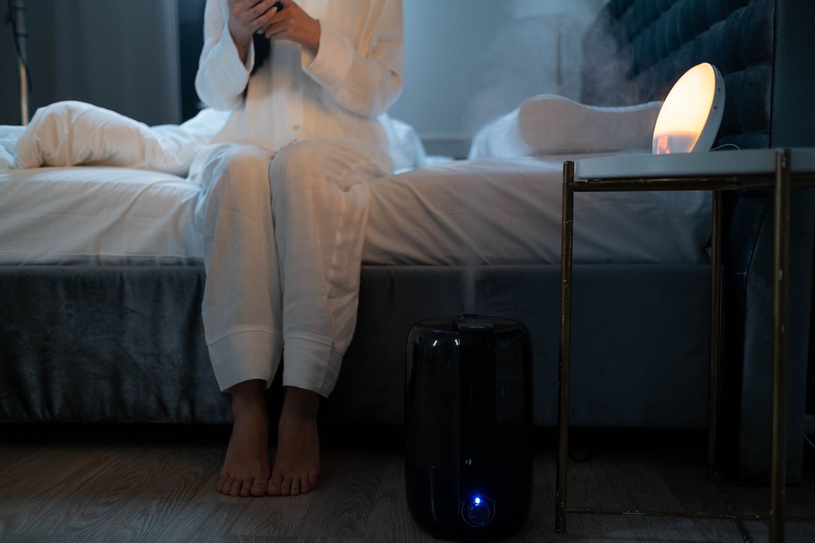 A cool mist humidifier running beside a bed in a dim room at night