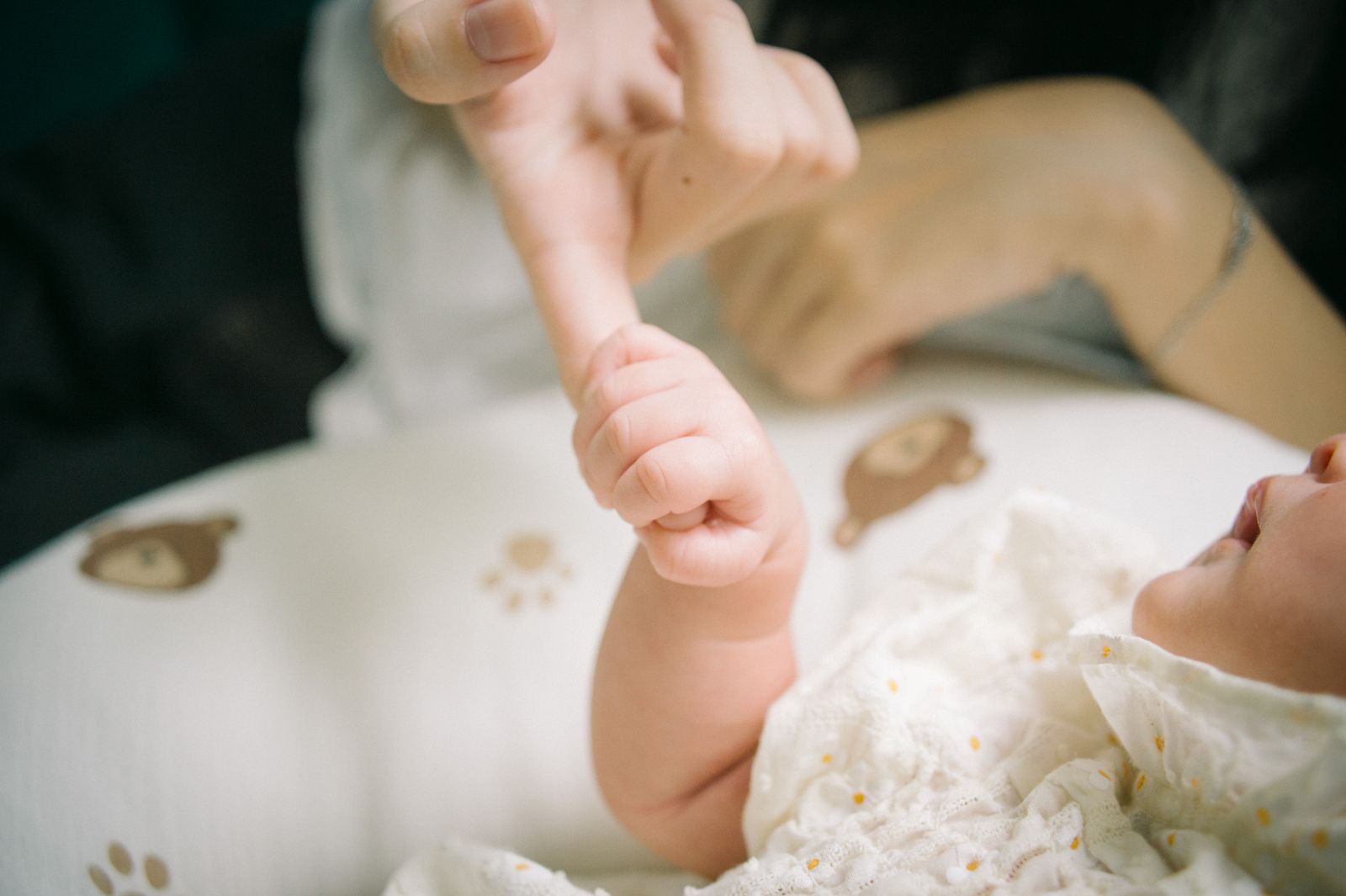 Newborn's tiny hand curled around a parent's finger on a soft blanket