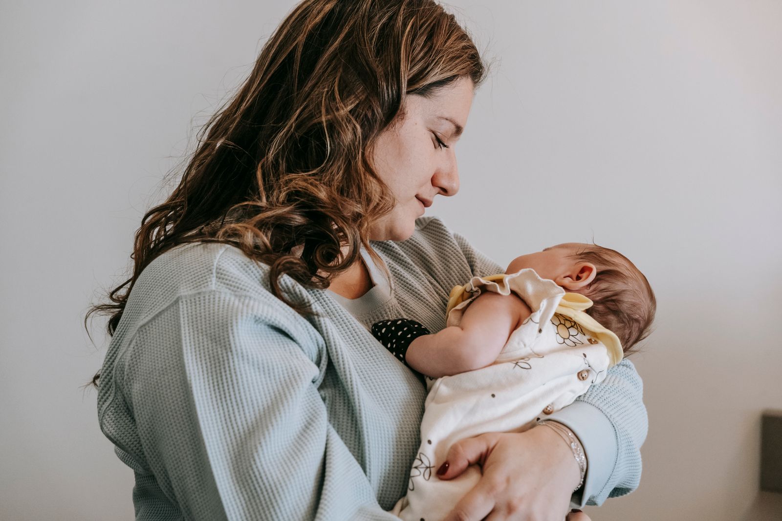 Mother holding her newborn upright against her chest in a calm, sunlit room