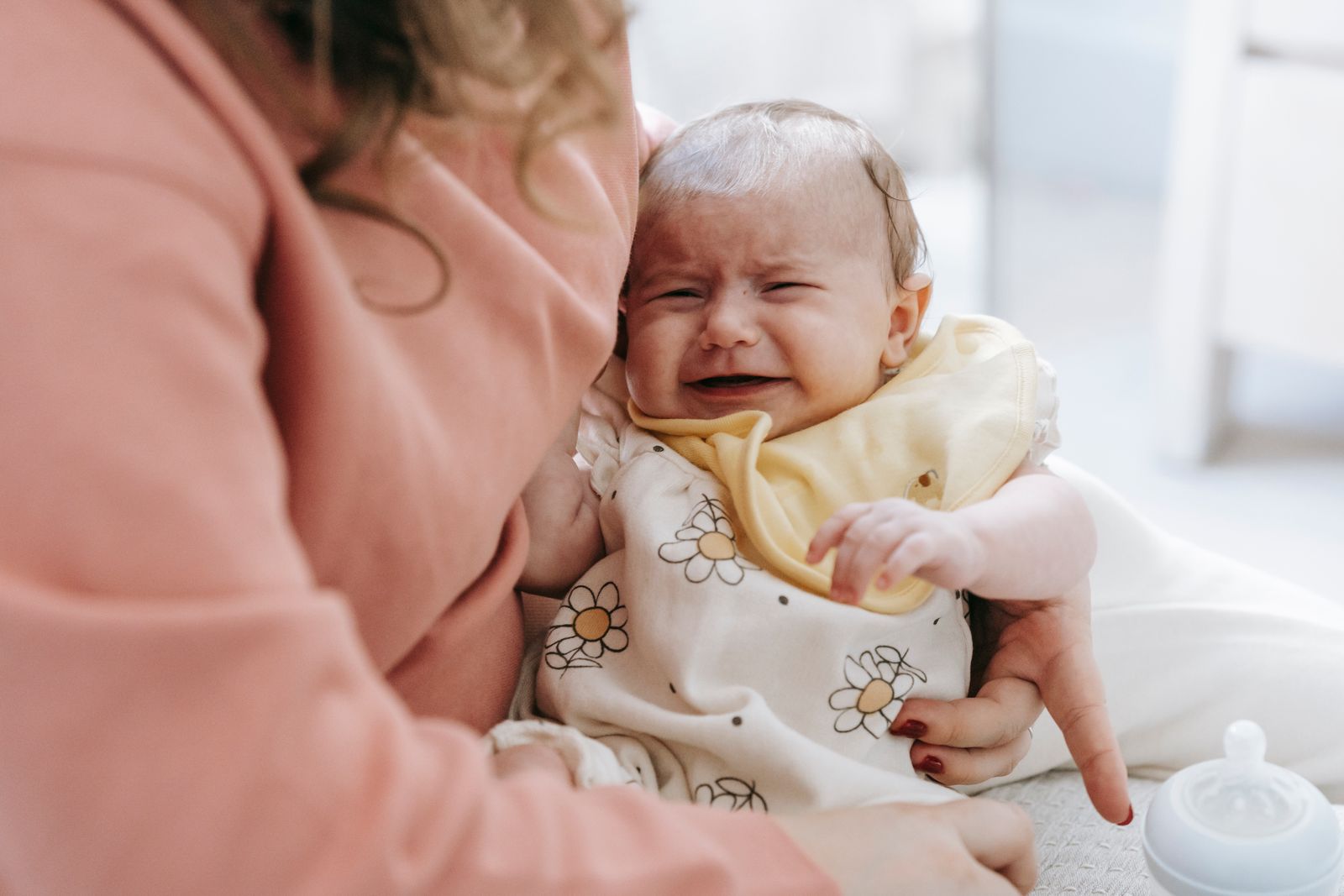 Baby crying in a mother's arms while sitting on a couch