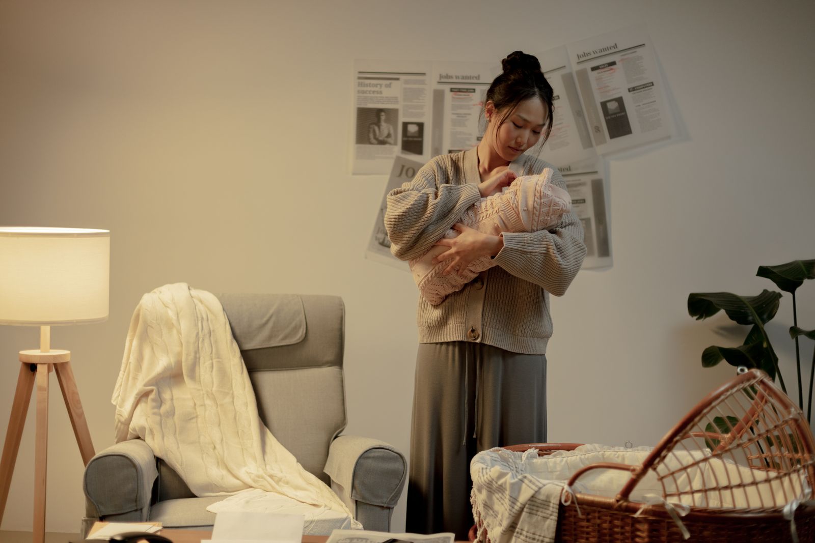A mother in a knit cardigan cradling her swaddled baby in a cozy dim room