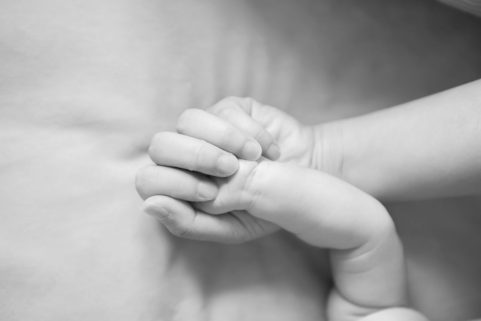 A black and white close-up of a newborn's hand wrapped around a parent's finger