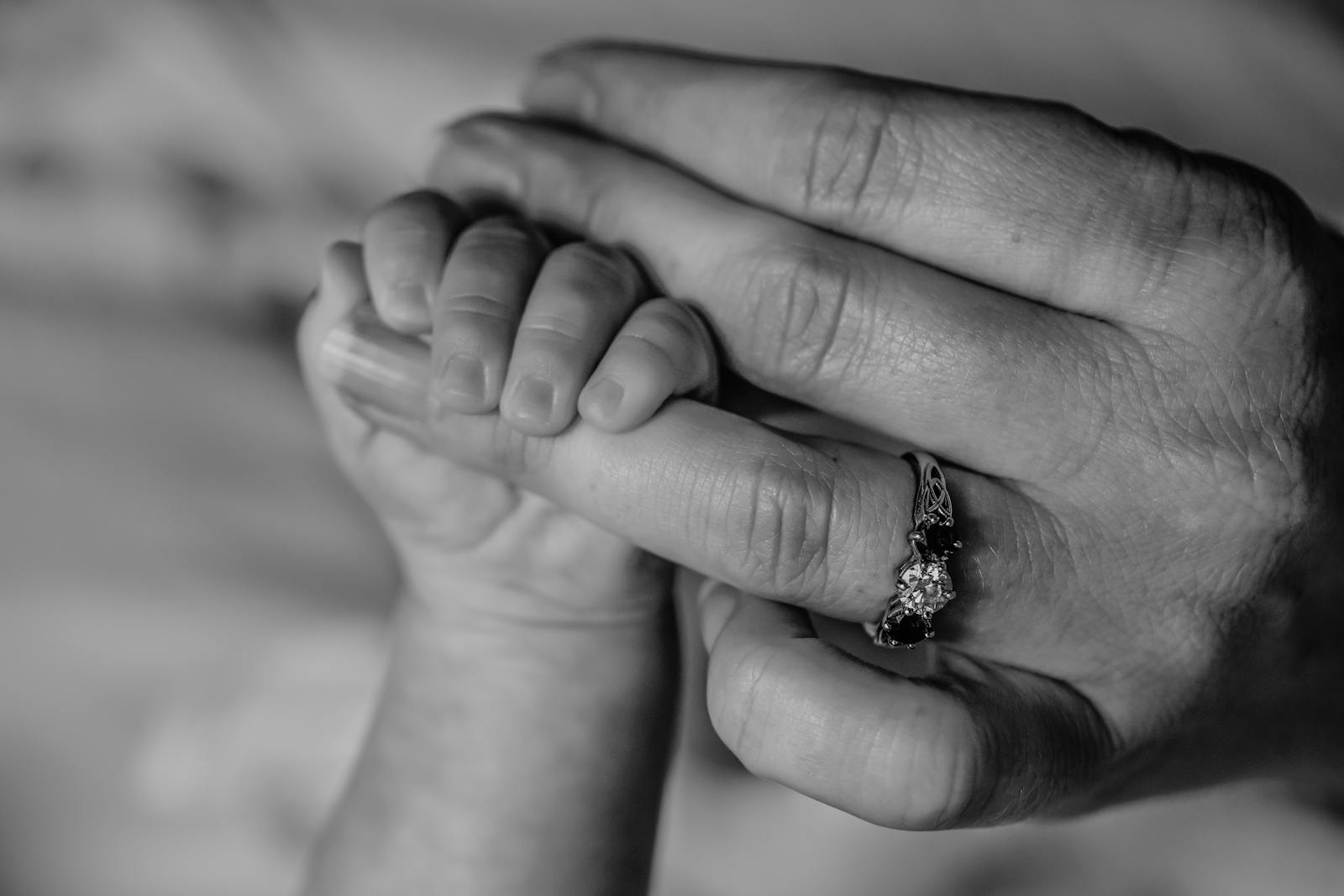 A newborn baby's hand wrapped around a parent's finger in a tender black and white close-up