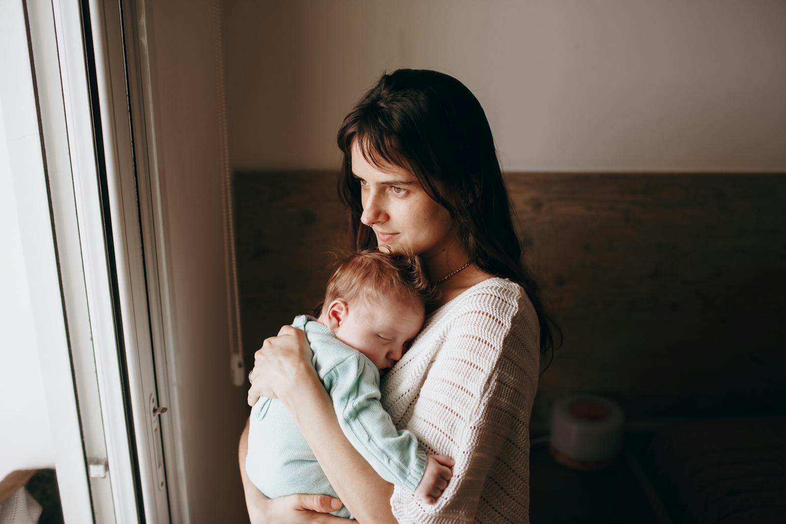 New mother in casual clothes holding her sleeping newborn close in a bright, peaceful home
