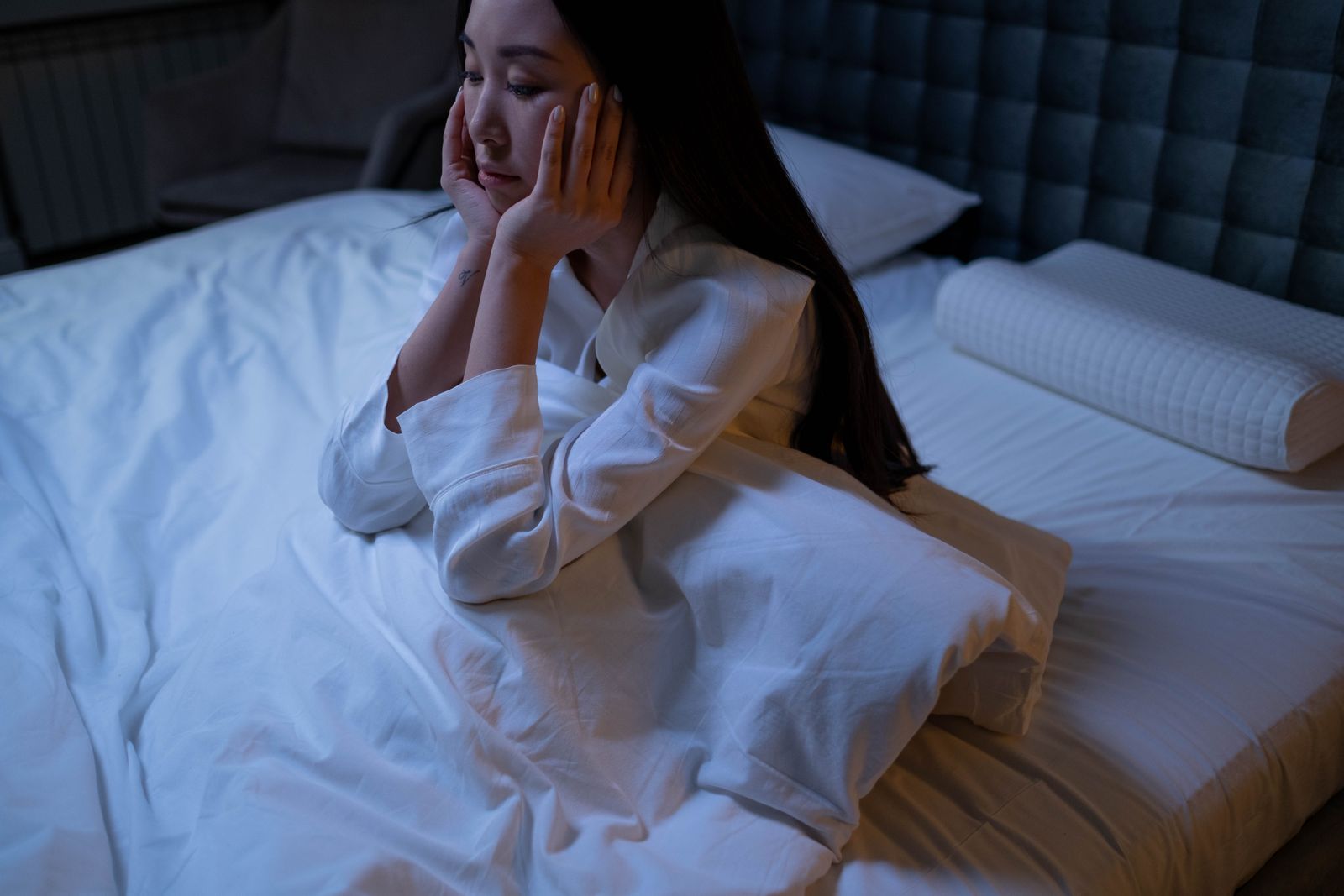 A woman sitting awake in bed at night, unable to sleep, hands to her face