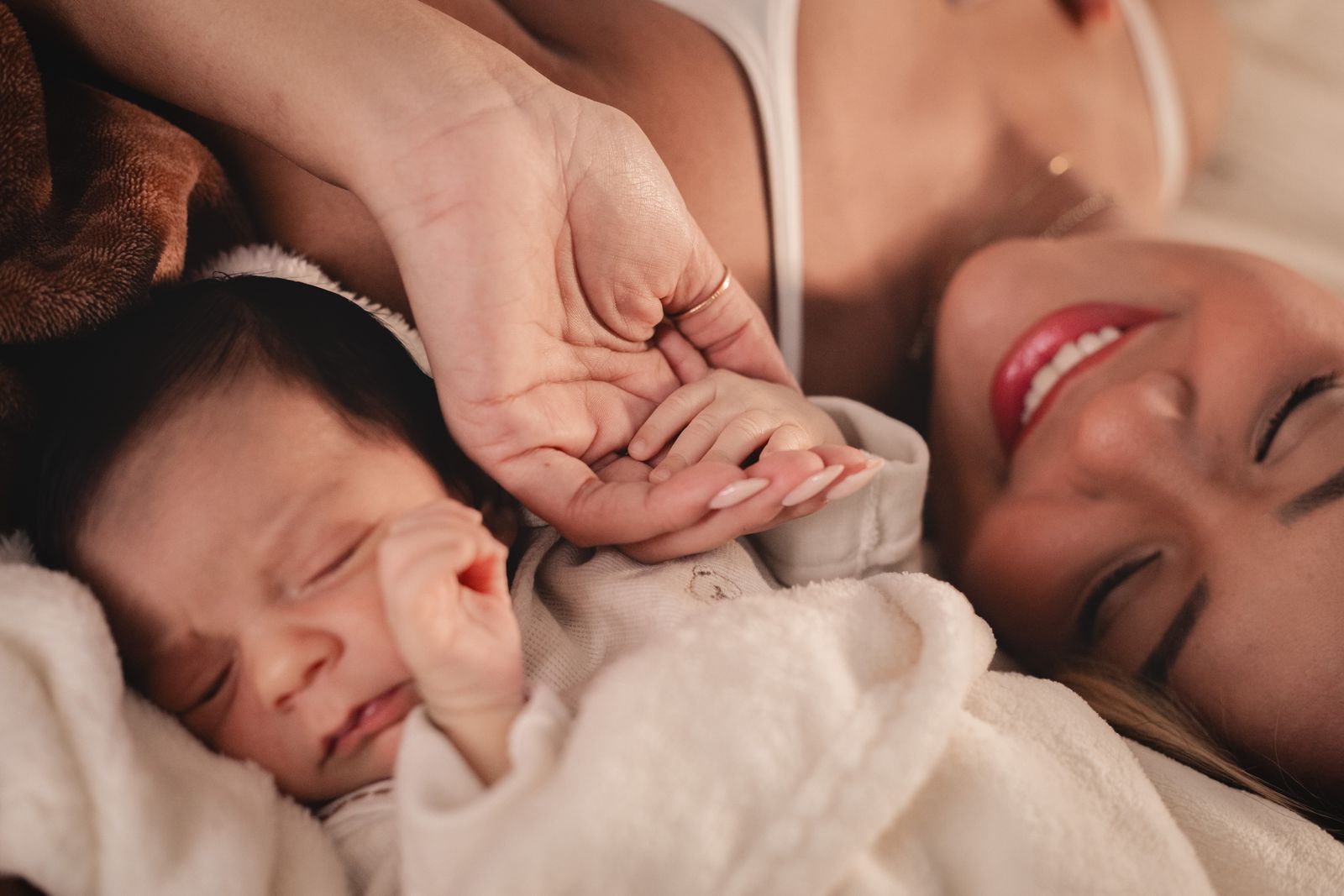 A parent lying beside their newborn, gently cradling the baby's tiny hand