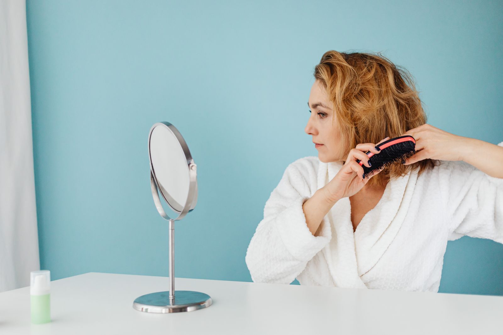 A hairbrush on a bathroom counter with several strands of hair caught in the bristles, soft morning light through a window