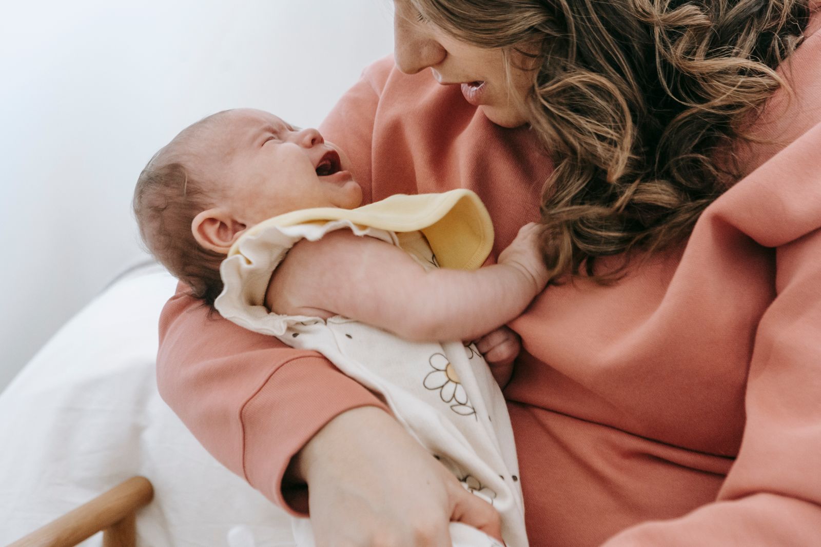 A mother holding her crying newborn, trying to soothe the baby