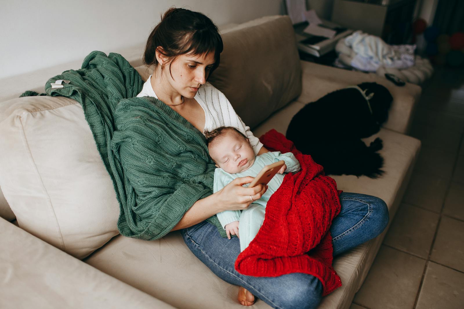 Mother resting on a couch with a blanket and sleeping baby, the postpartum recovery setup at home