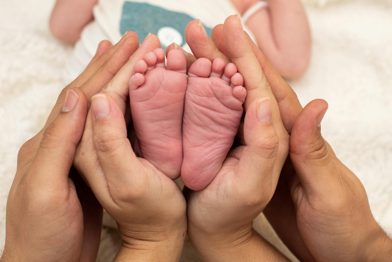 Tender close-up of a baby's feet cradled in a parent's hands, the emotional center of the postpartum recovery period