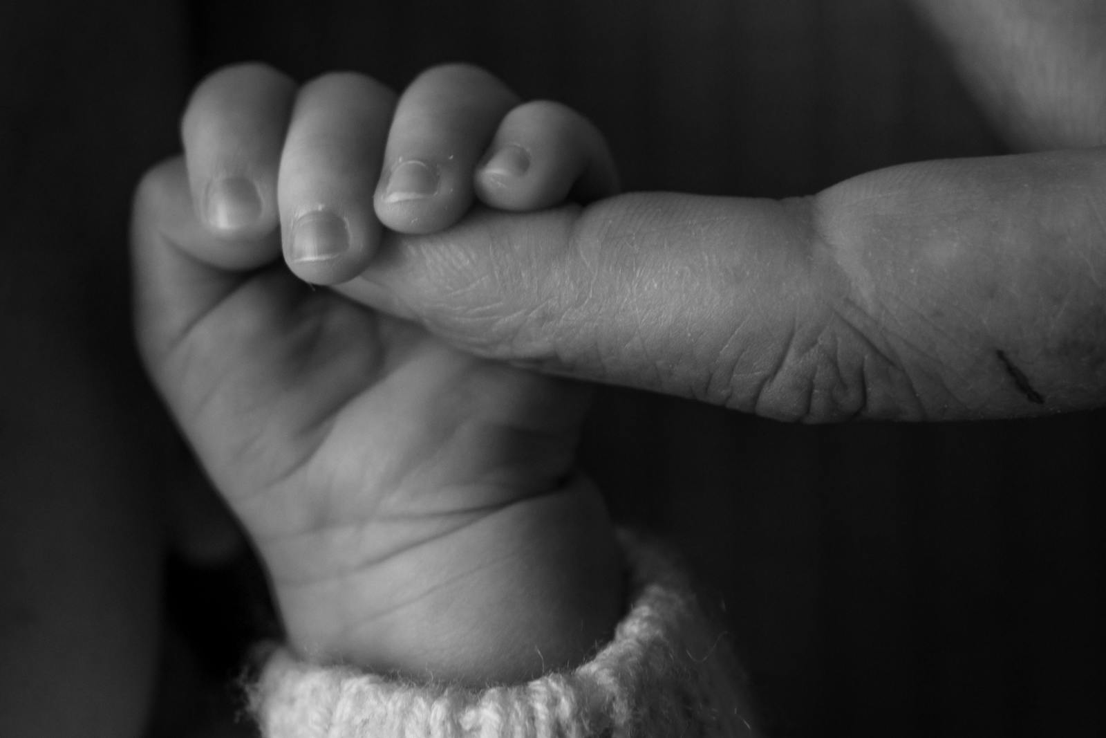 A small baby's hand gently held in an adult hand, in soft black and white tones