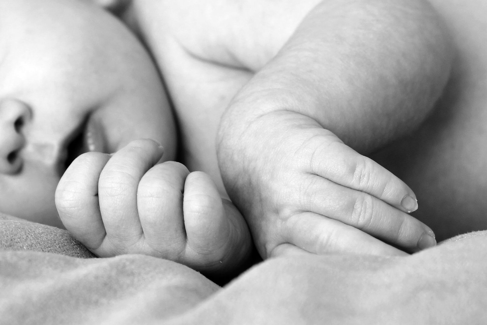 Black-and-white close-up of a small hand curled around an adult's finger, baby's face soft against a parent's shoulder