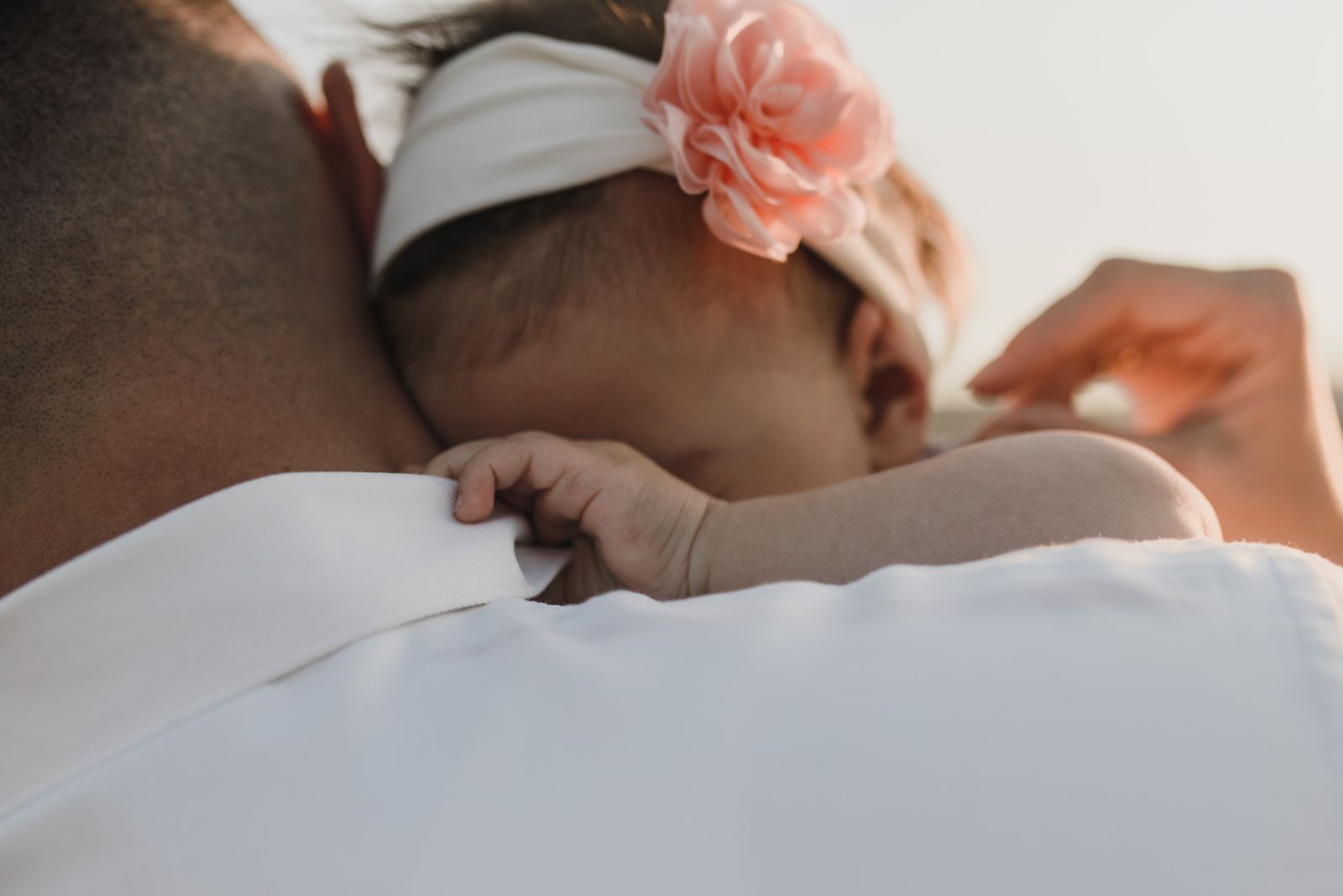 A baby resting on a parent's chest in an upright hold, mother's hand supporting baby's back, both faces calm