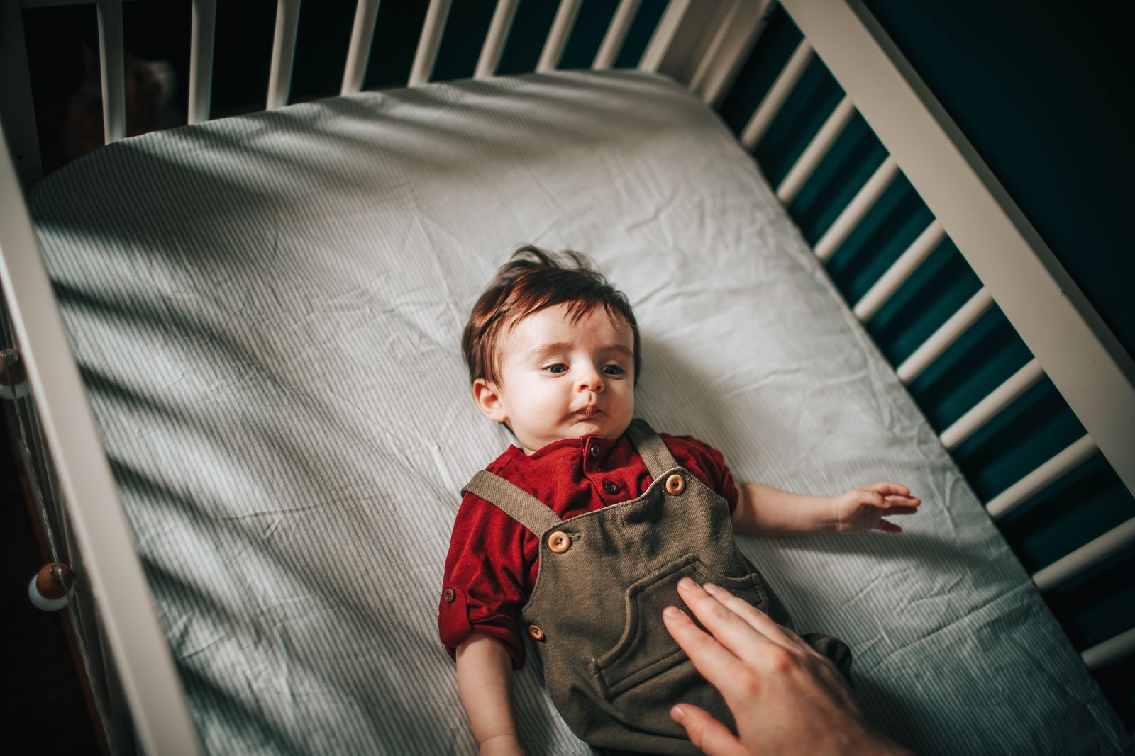 A parent's hand rests gently on a baby settling in the crib
