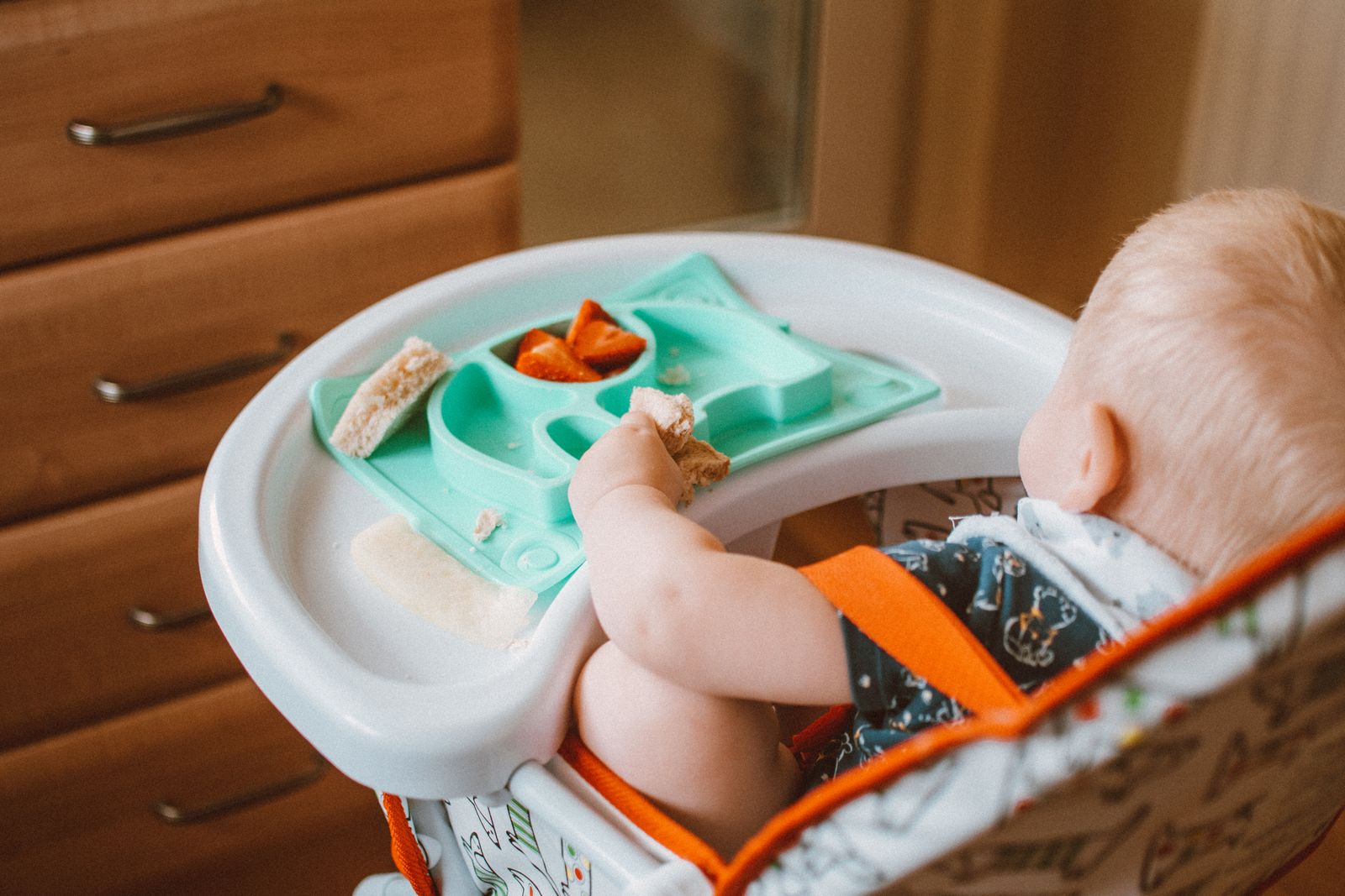 A baby self-feeding soft finger foods from a high chair tray