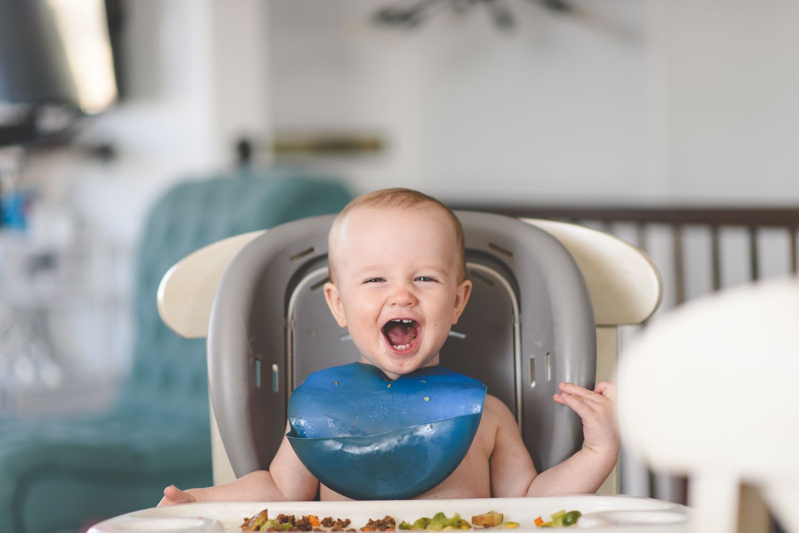 A baby laughing happily in a high chair during a meal