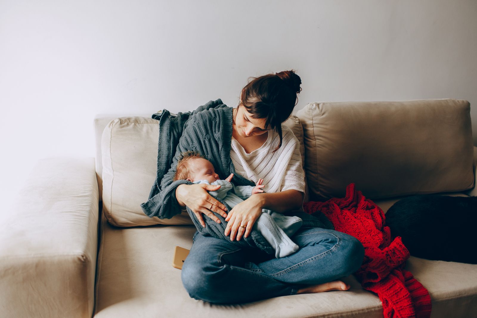 A mother sitting on a sofa holding her newborn close