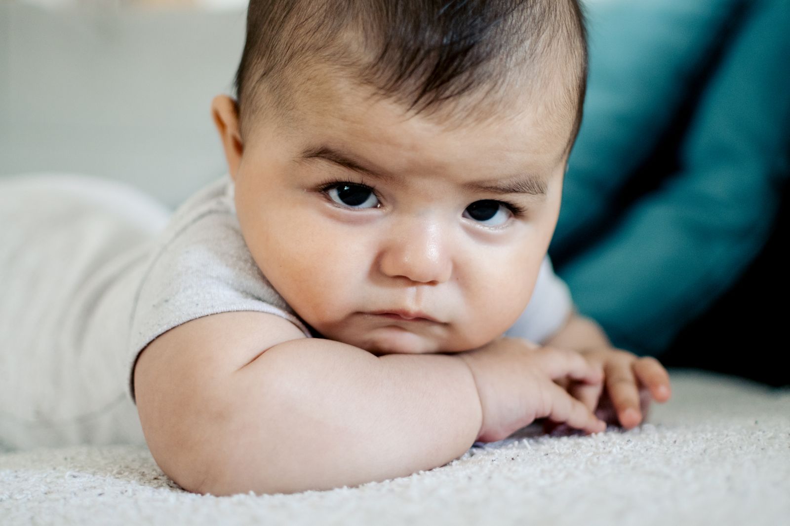 Baby lying on a soft white rug, resting on forearms with head lifted