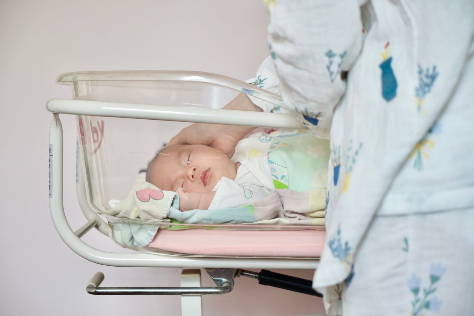 A calm parent lowering a drowsy baby into a bassinet, the baby's eyes half-closed, one small hand curled near the cheek