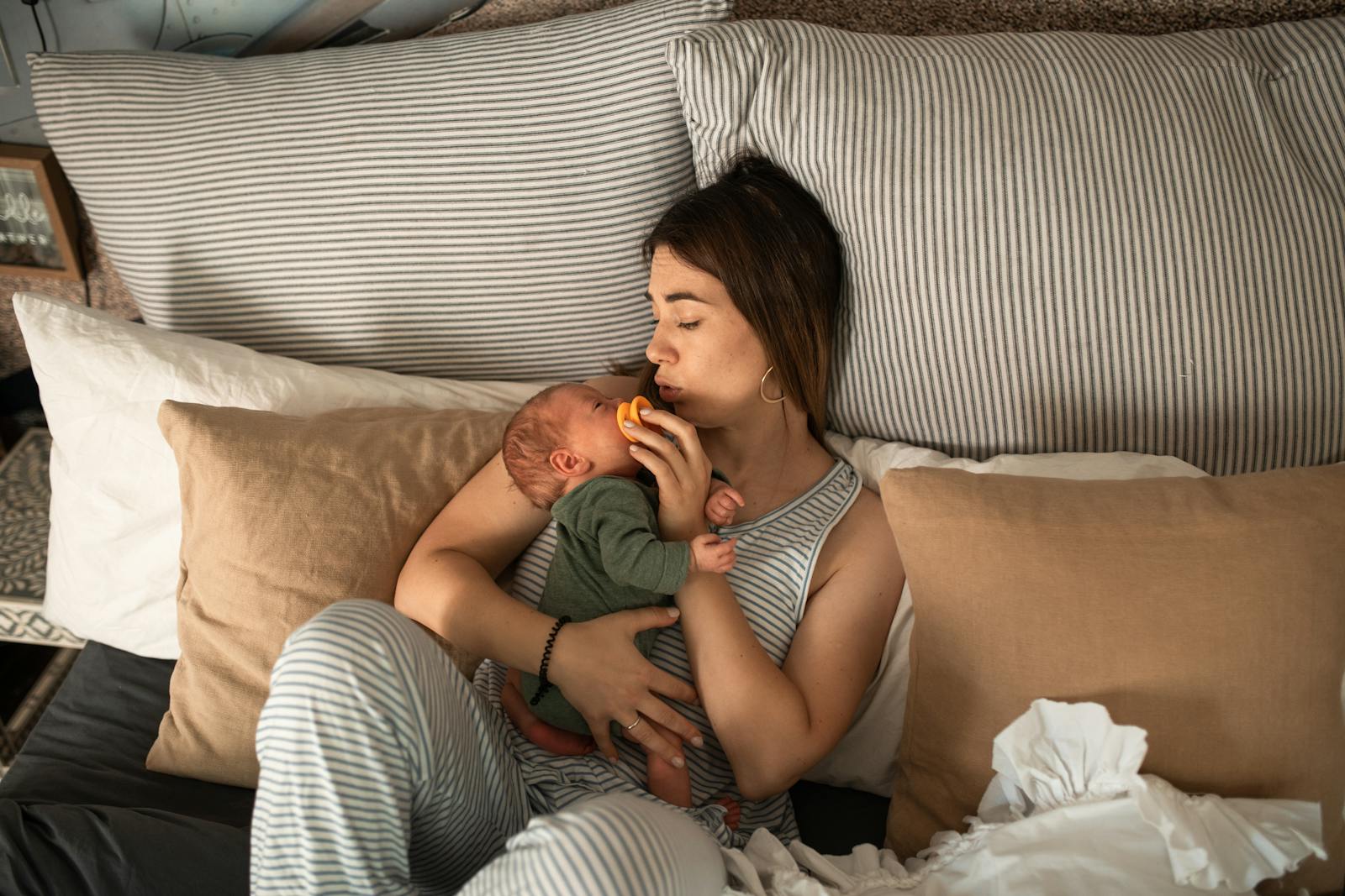 mom resting on bed holding newborn baby in postpartum recovery