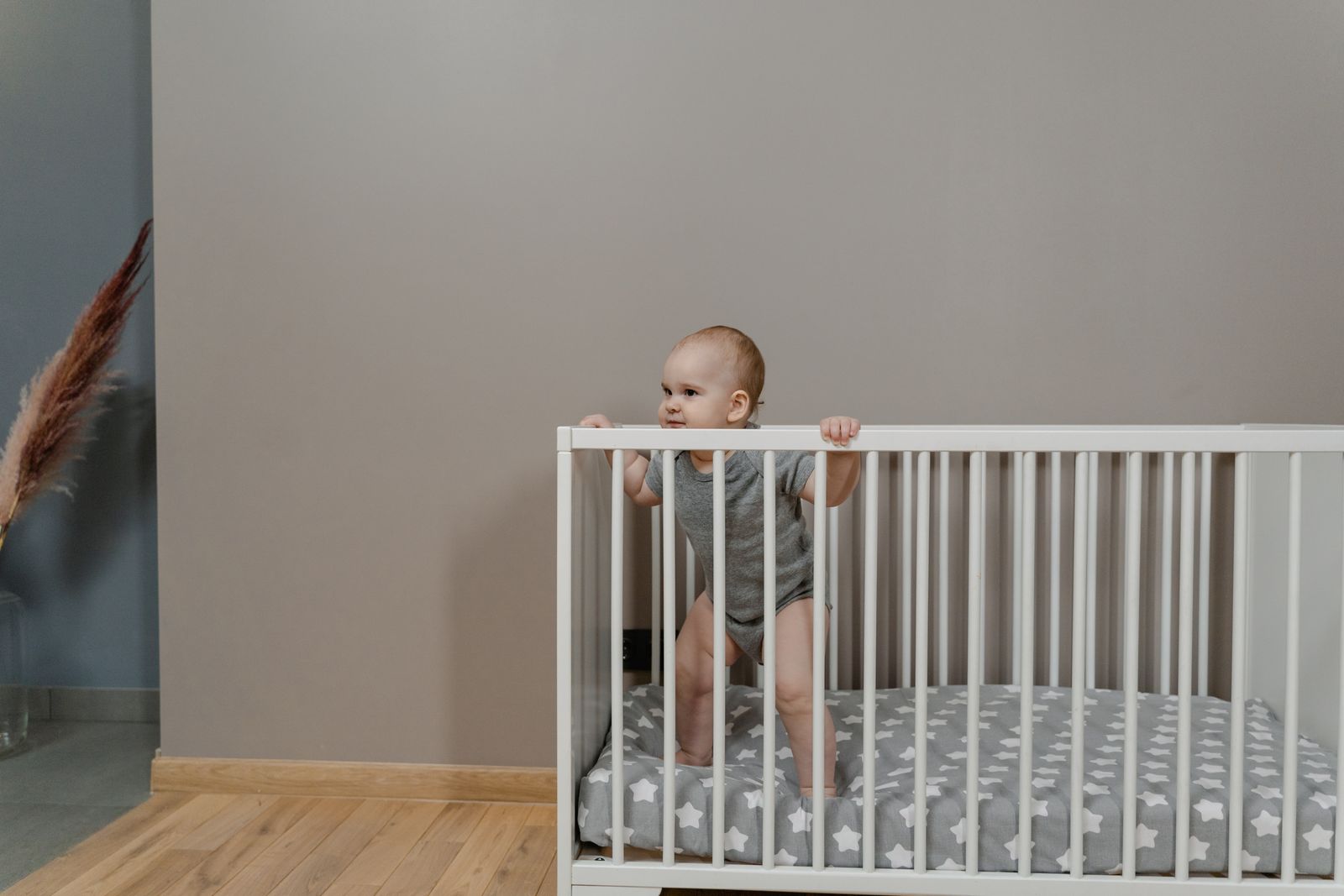 An older baby standing up and holding the rail of a crib
