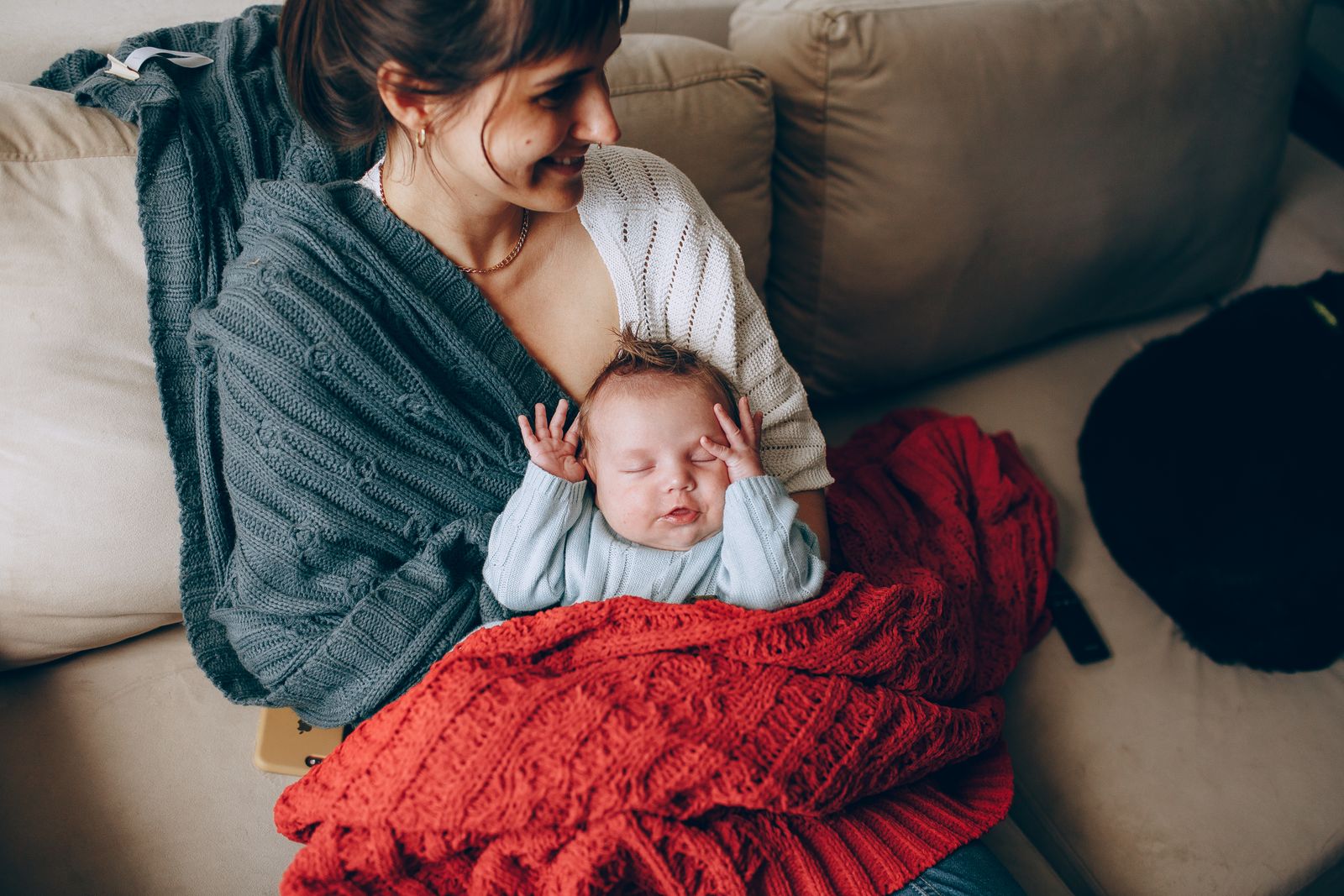 A mother smiling and holding her sleeping baby whose arms are up near their face